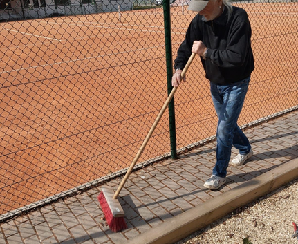 Teilnehmer kehrt Pflasterweg neben Bouleanlage mit rotem Besen beim Putzete 2025