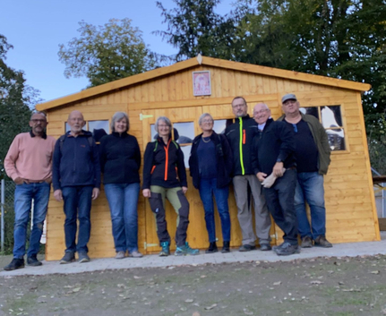 Acht Personen stehen vor einem hölzernen Gartenhaus im Freien