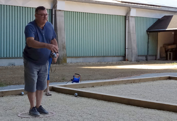 Mann im Wurfring wirft Boule auf Kiesbahn