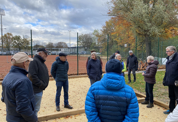 Personengruppe in Jacken neben umzäunten Tennisplätzen Schild 20