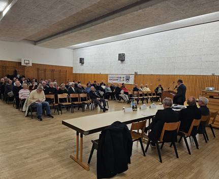Mitgliederversammlung in Sporthalle mit sitzendem Publikum und Vortragendem
