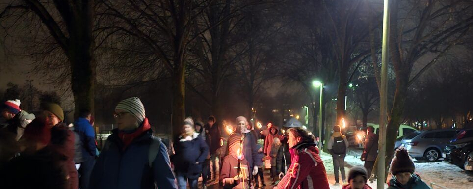 Kinder und Eltern mit Fackeln beim Winterspaziergang auf verschneiter Straße