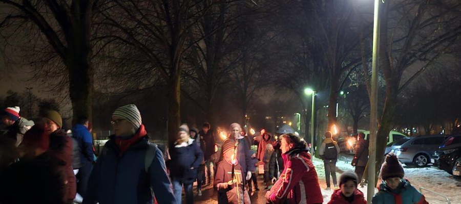 Kinder und Eltern mit Fackeln beim Winterspaziergang auf verschneiter Straße