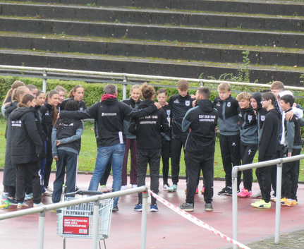 Einschwören auf die Mission "Sweep" Jugendliche Leichtathleten im Teamkreis mit Trainern auf nassem Belag