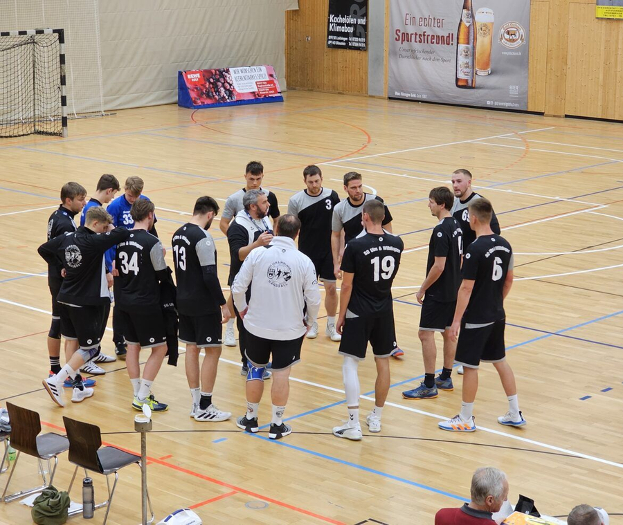 Männliche Handballspieler in schwarz mit Trainer im Hallenkreis
