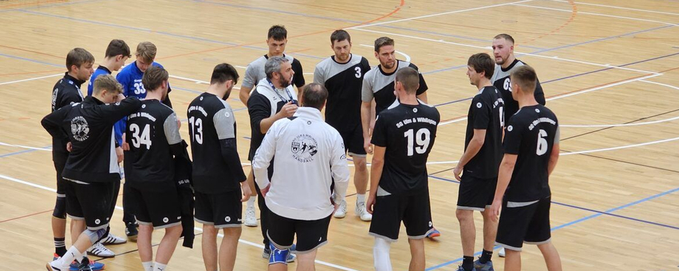 Männliche Handballspieler in schwarz mit Trainer im Hallenkreis
