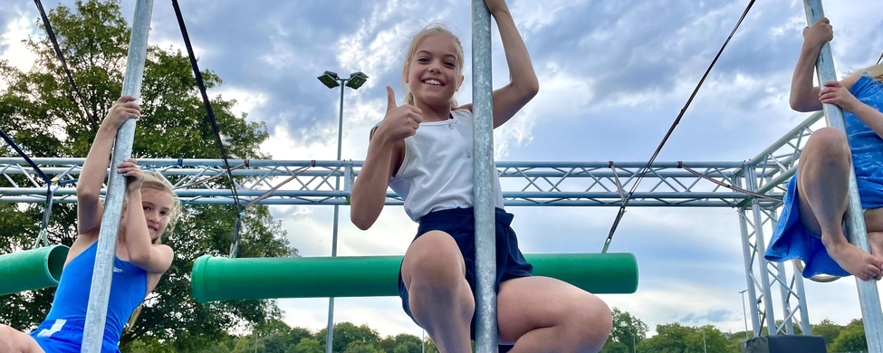 Ninja Warrior Wettkampf powered by Sparkasse Ulm 2024 Drei Kinder an Metallstangen auf Sportplatz mittleres zeigt Daumen hoch