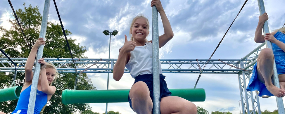 Drei Kinder an Metallstangen auf Sportplatz mittleres zeigt Daumen hoch