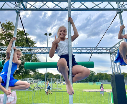 Ninja Warrior in Ulm - SSV Ulm 1846 e.V. Drei Kinder an Metallstangen auf Sportplatz mittleres zeigt Daumen hoch
