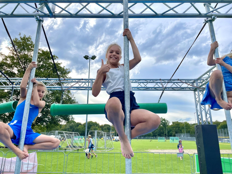 Drei Kinder an Metallstangen auf Sportplatz mittleres zeigt Daumen hoch