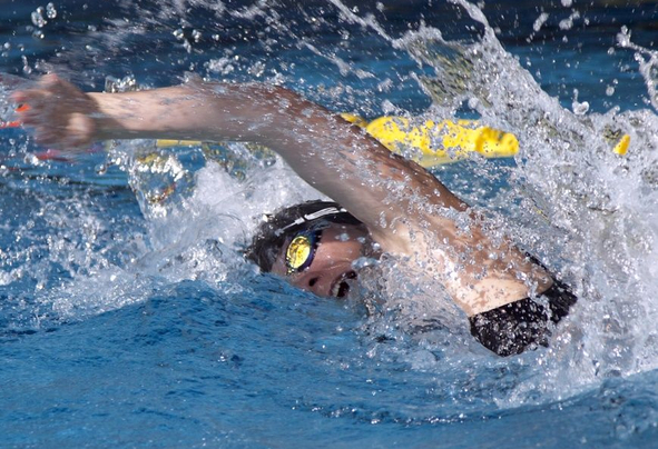 Person mit Schwimmbrille und Badekappe beim Schwimmen, spritzendes Wasser
