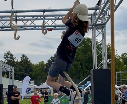 Kind klettert an Seil in Hindernisparcours mit Startnummer 60