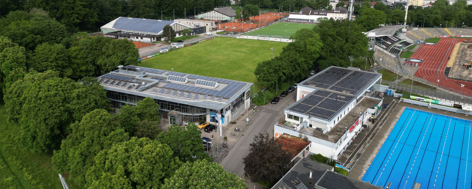 Luftaufnahme Stadiongelände mit Rasenplatz, Tribüne, Parkplätzen und Außen-Schwimmbecken