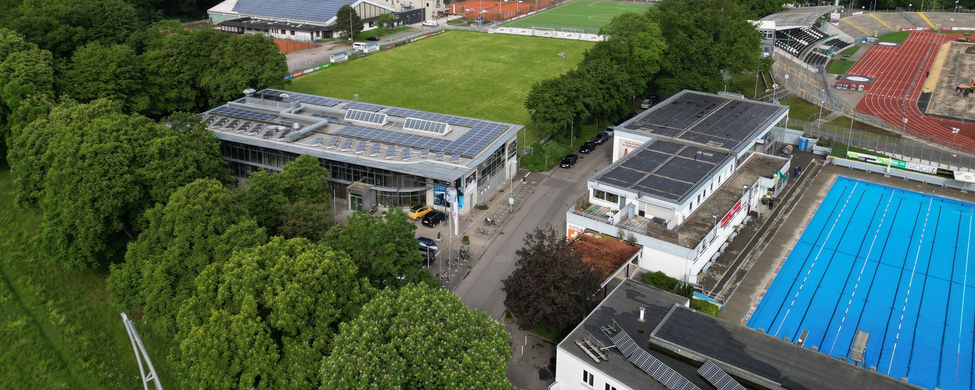 Luftaufnahme Stadiongelände mit Rasenplatz, Tribüne, Parkplätzen und Außen-Schwimmbecken