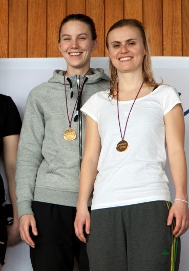 Vier lächelnde Frauen mit Medaillen vor Banner