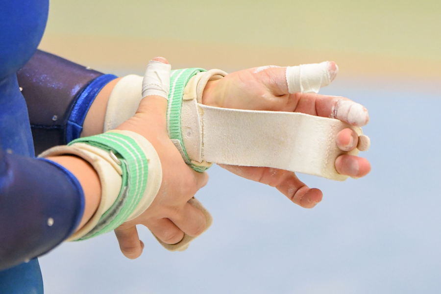 Turnerin befestigt Griffriemen am Handgelenk mit getapten Fingern und Kreide