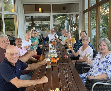 Gruppe von älteren Erwachsenen auf Terrasse am langen Tisch beim Anstoßen