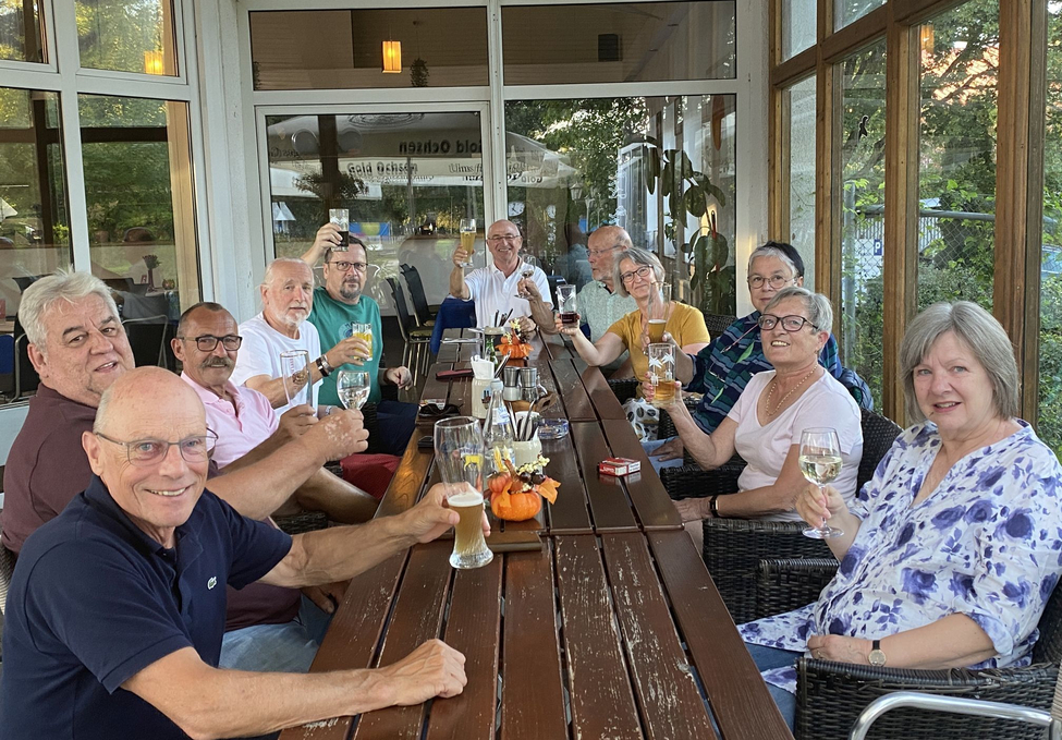 Gruppe von älteren Erwachsenen auf Terrasse am langen Tisch beim Anstoßen