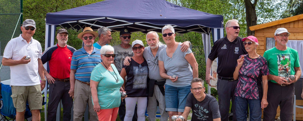 Gruppe älterer Menschen posiert vor Pavillon mit Boulekugeln