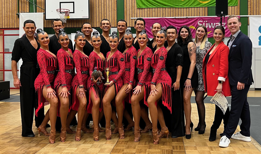 Formationstanzteam in roten Kostümen mit Pokal in Sporthalle