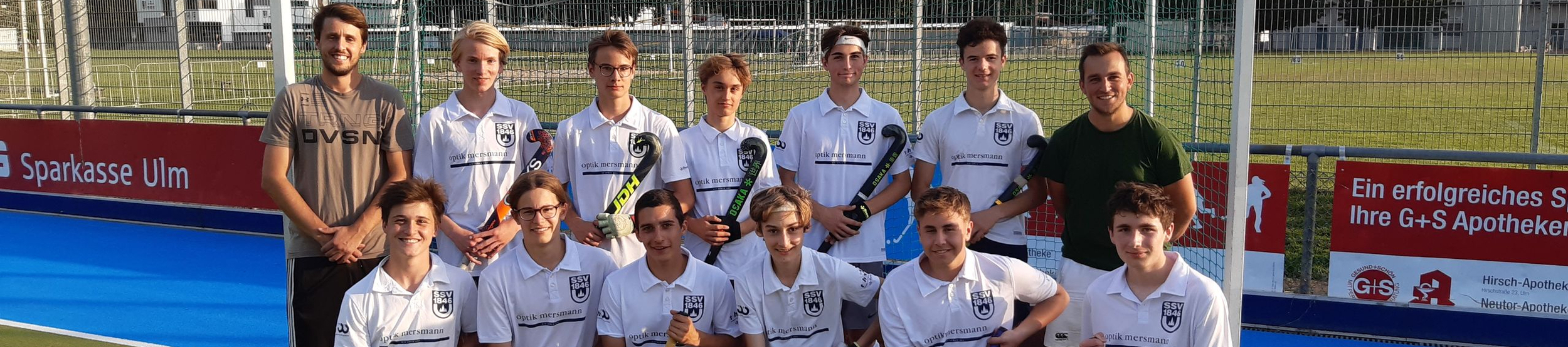 Jugend-Hockeymannschaft in weißen Trikots vor Tor mit Hockeyschlägern