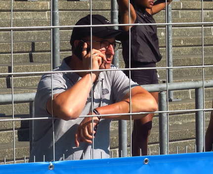 Mann mit Kappe und Smartphone lehnt am Absperrgitter im Stadion