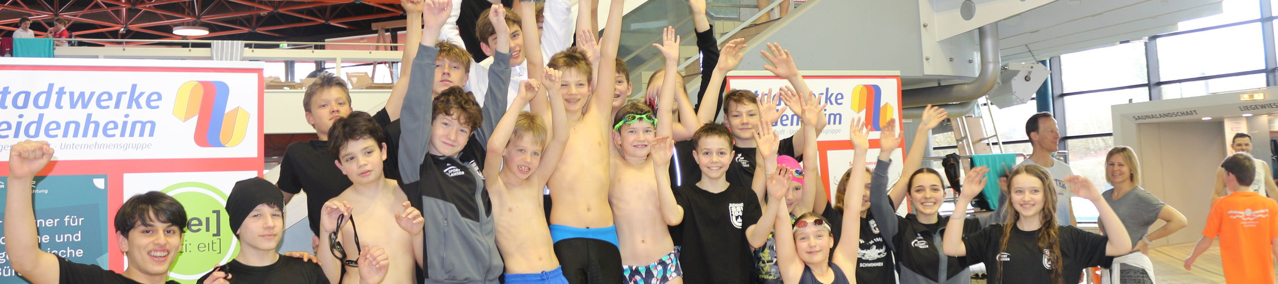Jugendliche Schwimmer auf Siegerpodest halten Pokal und jubeln