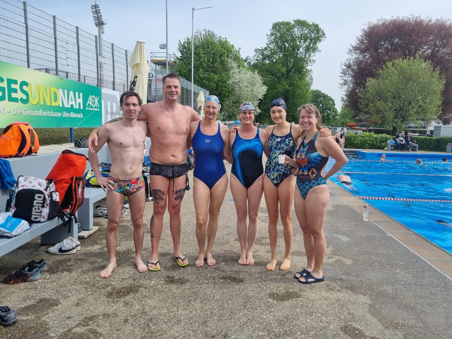 Sechs Schwimmerinnen und Schwimmer in Badebekleidung am Freibadbeckenrand