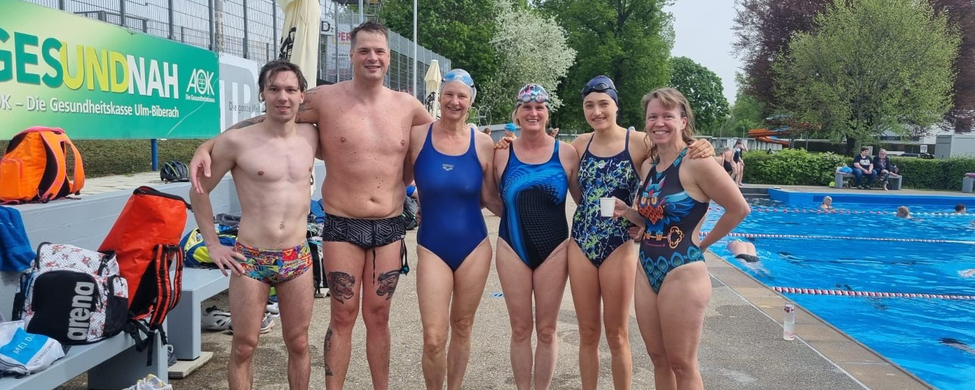 Sechs Schwimmerinnen und Schwimmer in Badebekleidung am Freibadbeckenrand