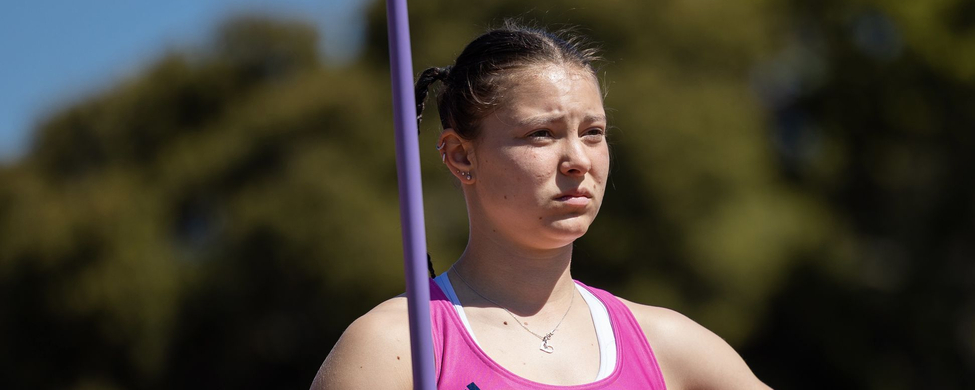 Athlete in pink Nevada singlet holding purple javelin pole