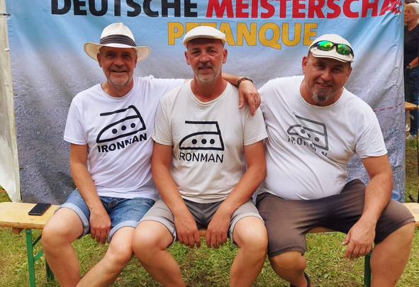 Drei Männer sitzen vor Banner Deutsche Meisterschaft Petanque
