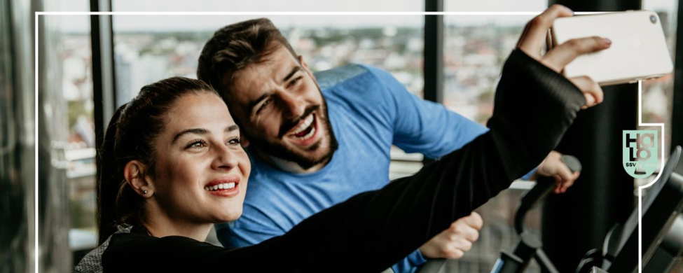 Zwei lächelnde Personen machen Selfie auf Cardiogerät mit Fensterblick