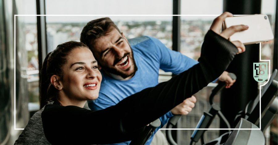 Zwei lächelnde Personen machen Selfie auf Cardiogerät mit Fensterblick
