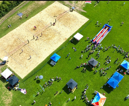 Luftaufnahme einer Wiese mit Sand-Volleyballfeldern, Zelten, aufblasbarer Rutsche