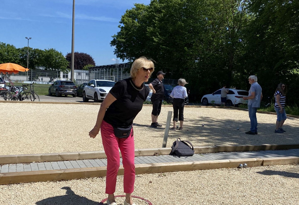Frau in schwarzem Shirt und pinker Hose spielt Boule im Kreis