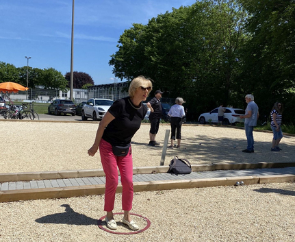 Frau in schwarzem Shirt und pinker Hose spielt Boule im Kreis