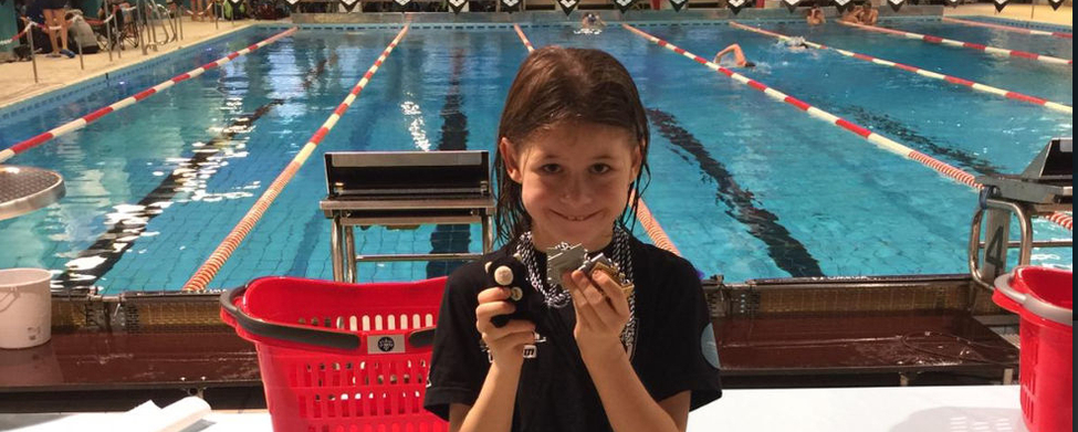 Kind vor Schwimmbecken hält Medaillen und kleine Trophäe