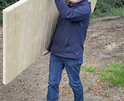 Mann trägt große Holzplatte im Freien lächelnd