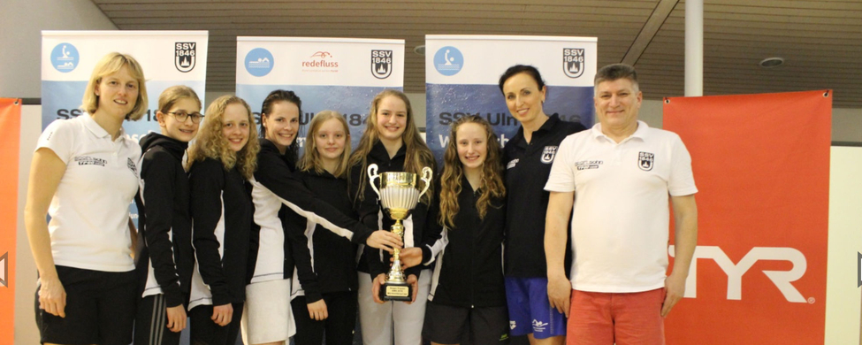 Jugendliches Schwimmteam stehend hält großen Siegerpokal