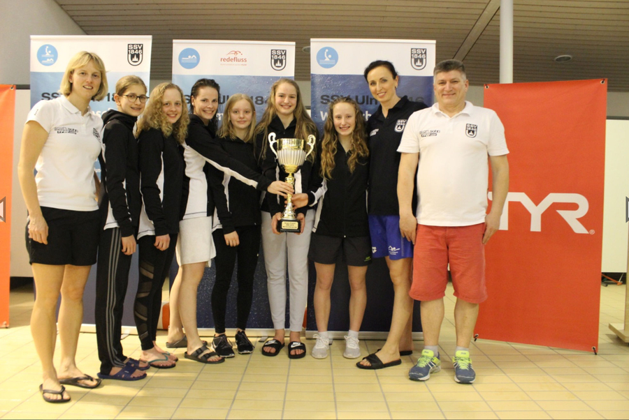 Jugendliches Schwimmteam stehend hält großen Siegerpokal