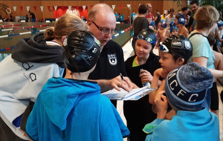 Trainer mit Klemmbrett bespricht Zeiten mit jungen Schwimmern