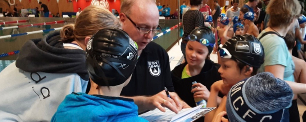 Trainer mit Klemmbrett bespricht Zeiten mit jungen Schwimmern
