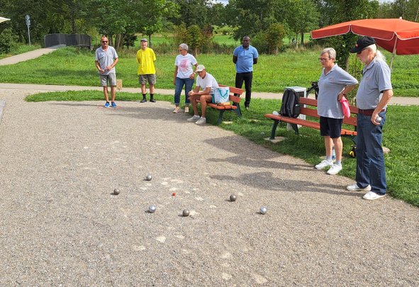 Personen spielen Boule auf Kiesbahn mit Kugeln um rote Zielkugel