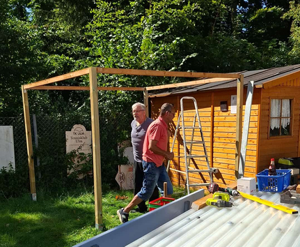 Zwei Männer montieren Holzrahmen neben Vereinshütte Schild Tennisklub Ulm