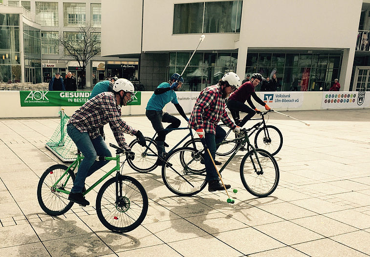 Vier Personen spielen Fahrradpolo auf städtischem Platz