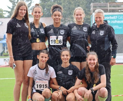 Jugendliches Leichtathletikteam mit Medaillen auf Podest im Regen Startnummer 1915