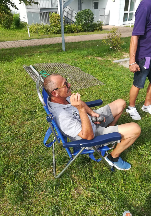 Mann mit Sonnenbrille sitzt im blauen Klappstuhl auf Gras hält Metallkugeln