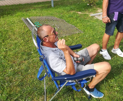 Mann mit Sonnenbrille sitzt im blauen Klappstuhl auf Gras hält Metallkugeln
