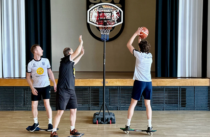 Drei Personen auf Skateboards werfen Basketball in Halle