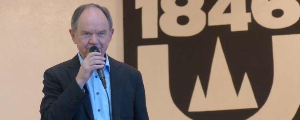 Älterer Mann spricht ins Mikrofon vor SSV 1846 Wappen
